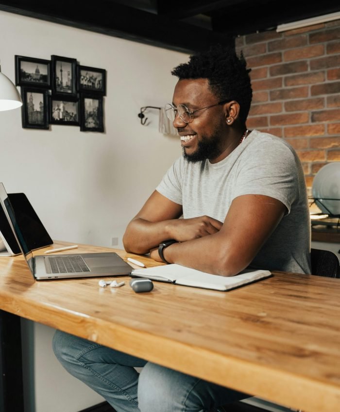African American man smiling and working remotely from home using a laptop and digital tablet.